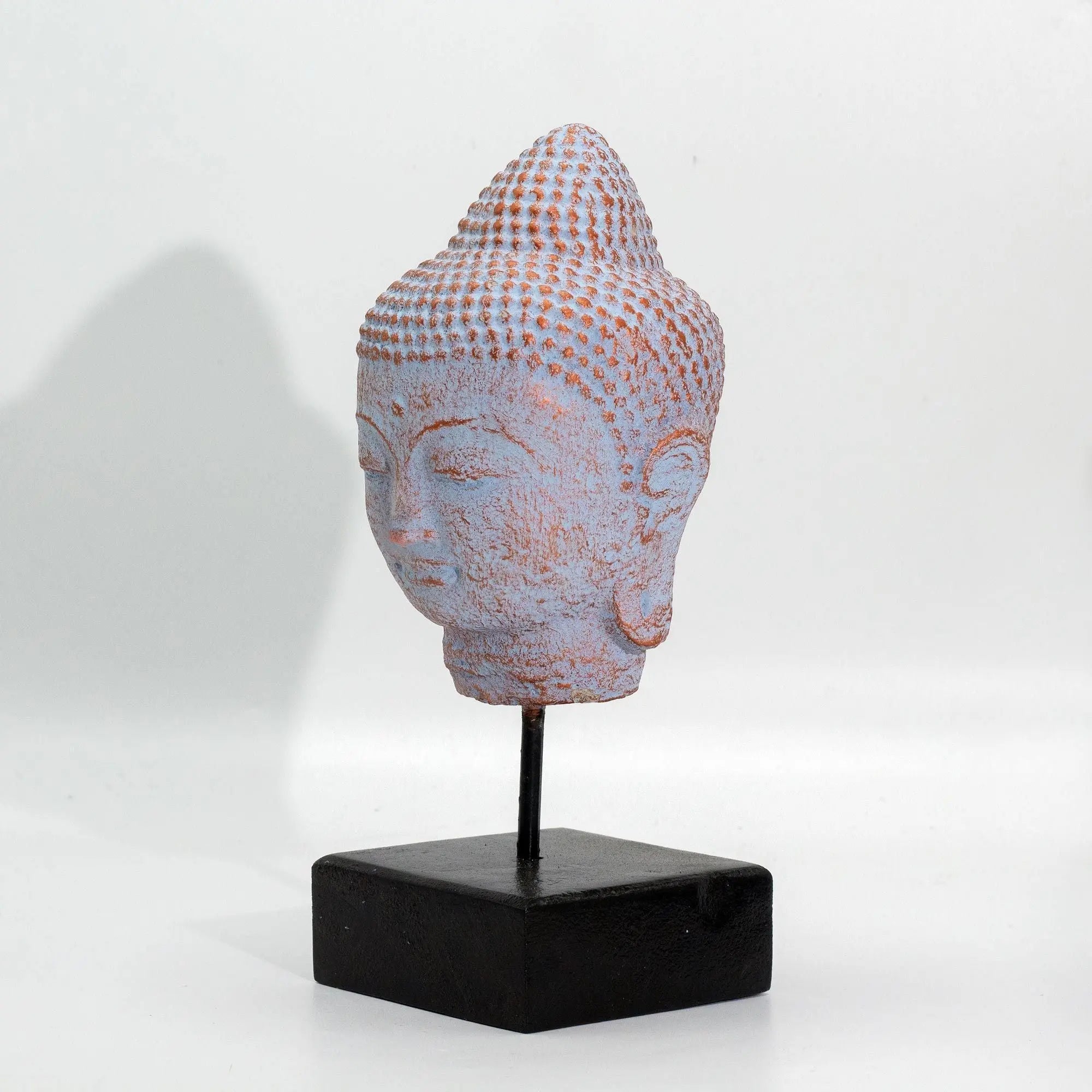 Stillness Buddha Head on Stand - Blue Copper displayed on a black square base, showcasing a textured blue copper finish with serene facial features and detailed hair curls.
