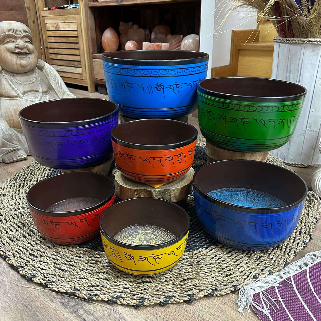 Large Chakra Set of Seven Singing Bowls (19.5-35cm) displayed on a woven mat with vibrant colors and engraved script, surrounded by calming home decor elements.