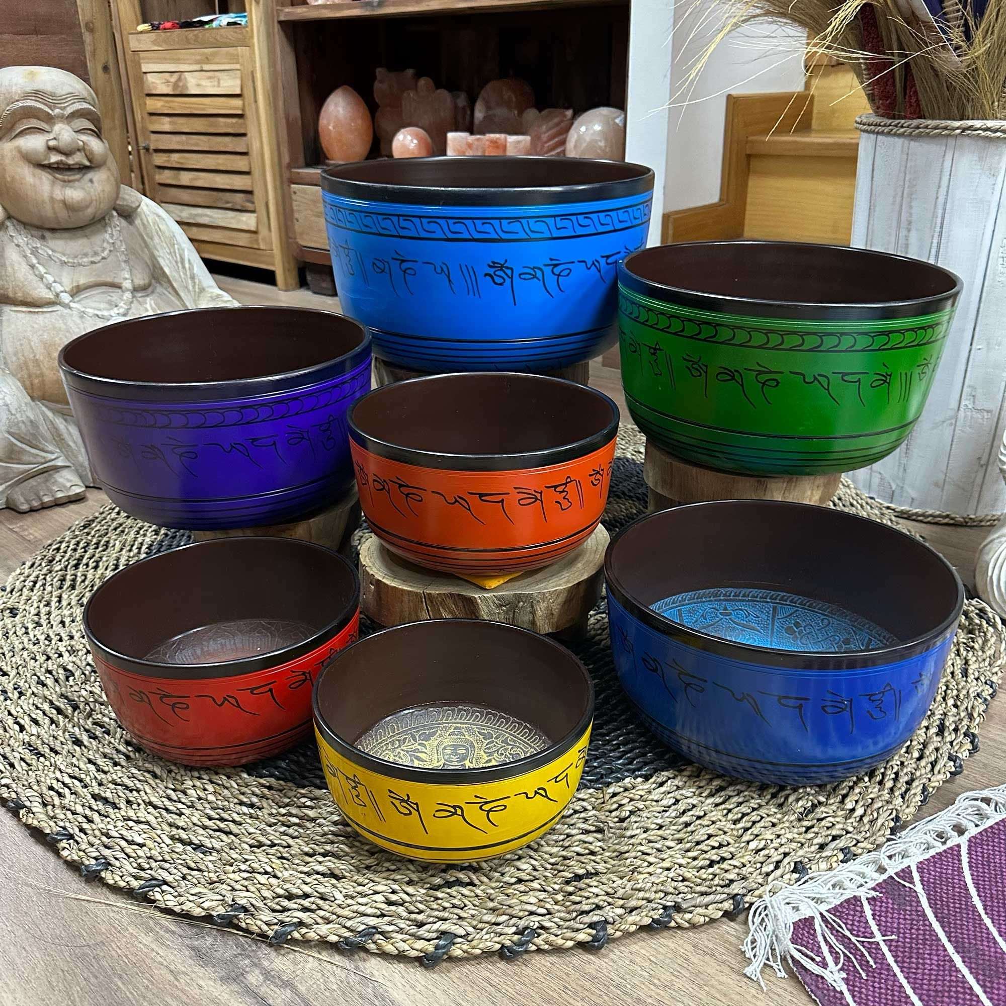Large Chakra Set of Seven Singing Bowls (19.5-35cm) displayed on a woven mat with vibrant colors and engraved script, surrounded by calming home decor elements.