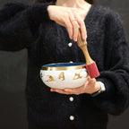 Person holding a Large Moon Phase Singing Bowl Set- Black 14cm with a wooden mallet, featuring moon phase designs around the bowl and a black interior.