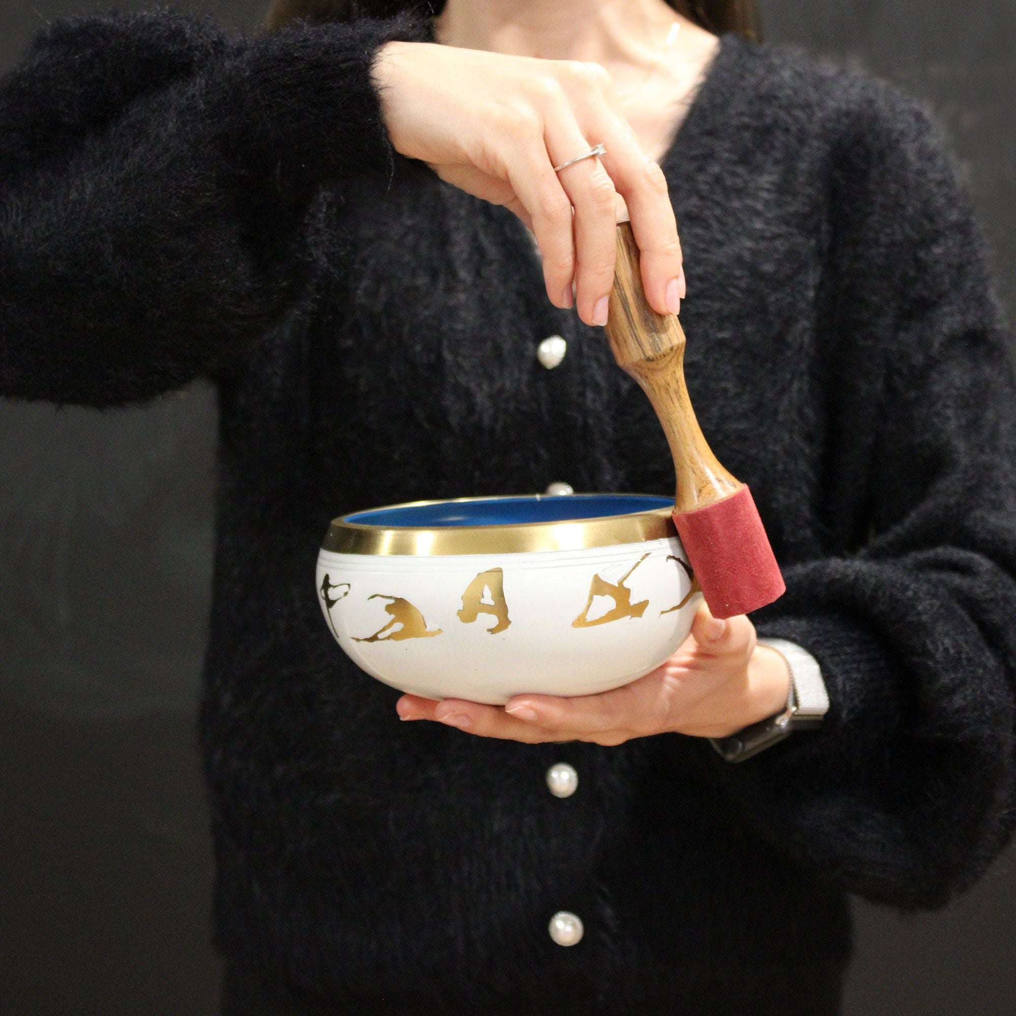 Person holding and playing a Large Tree of Life Singing Bowl Set- Green 14cm with a wooden mallet, wearing a black sweater with pearl buttons.