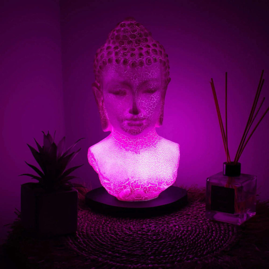 Buddha Bust Lamp Cherry Crackle - Oval stand glowing with soft pink light, displayed on a woven mat with a small plant and reed diffuser nearby, creating a serene ambiance.