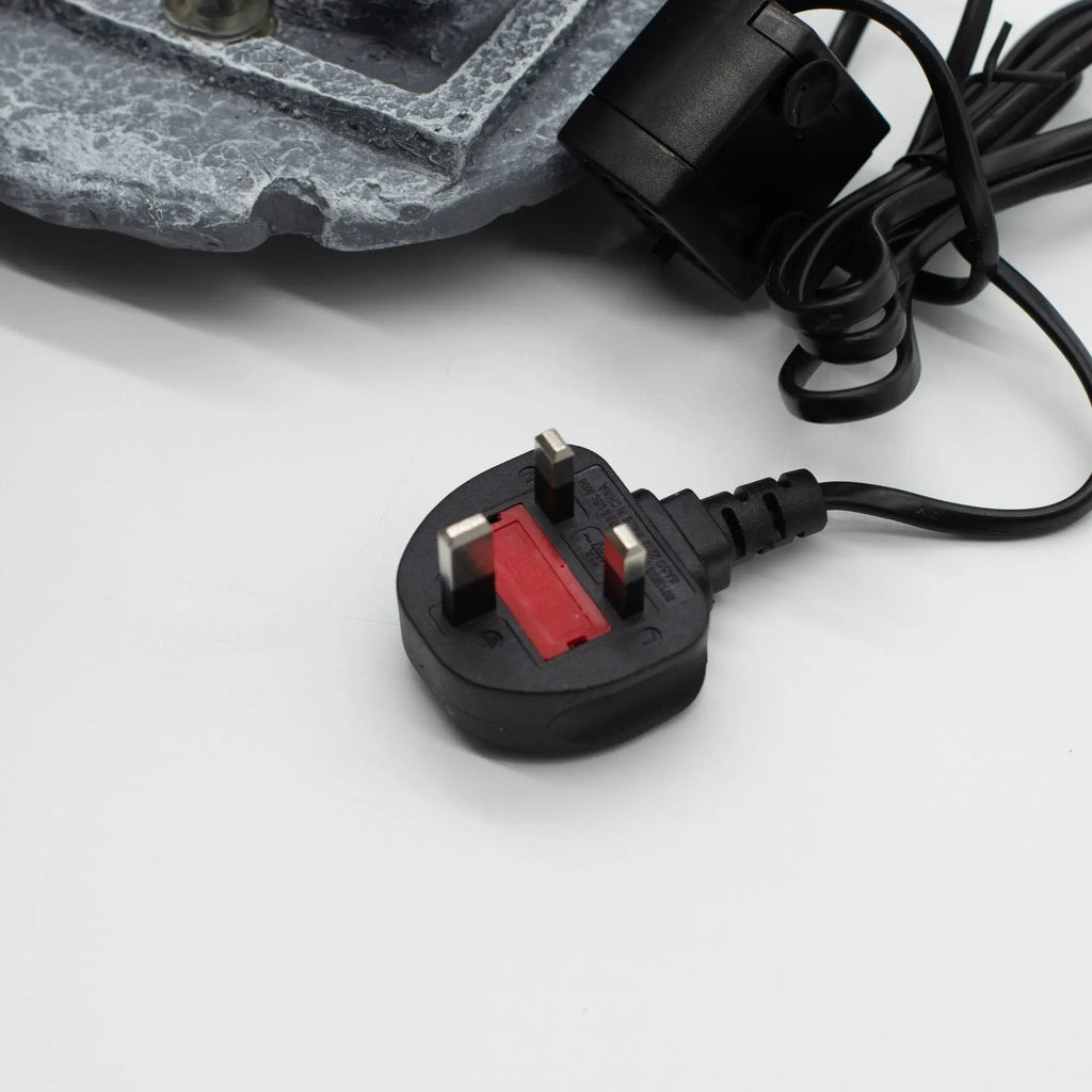 Close-up of a UK plug connected to the Tabletop Water Feature - 19x19x28cm - Buddha, Lotus Flower Cascading Potsx, showing part of the water feature base and electrical cord.