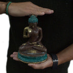 Person holding a Large Sitting Solid Brass Buddha with turquoise-colored hair and base, showing detailed craftsmanship and meditative posture in warm lighting.
