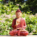 Hand Carved Buddha Statue - 30cm Teaching Transmission showing a serene meditative figure in red robes seated outdoors against a lush green background, evoking peaceful Buddha decor.