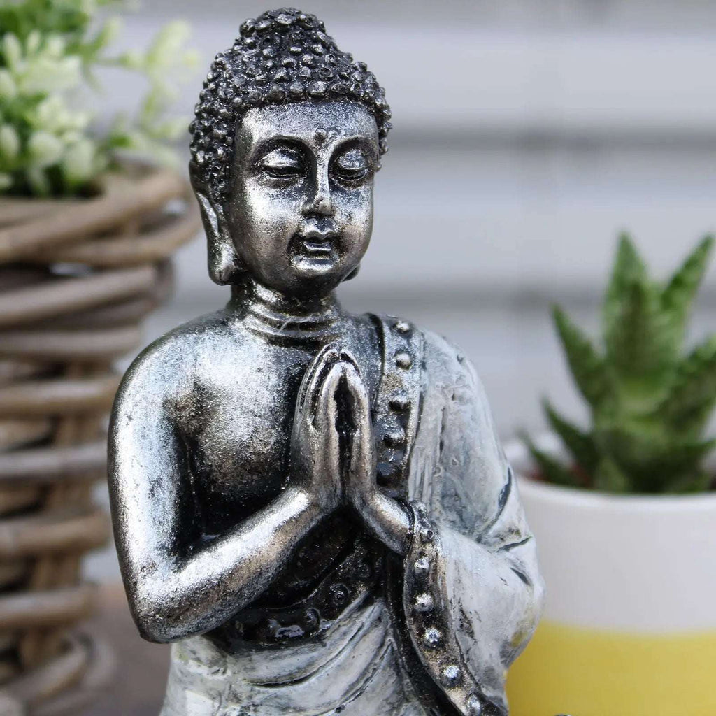 Close-up of a hand-carved Buddha statue with detailed facial features and textured hair, styled as a Buddha Candle Holder - White - Medium, placed among green plants.