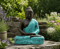Medium Buddha Classic Turquoise & Stone - 0.5m statue seated in meditation pose with a turquoise robe finish, placed outdoors on a stone surface surrounded by greenery and flowers.