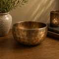 Large Nepalese Moon Bowl - (approx 850g) - 17cm made of polished metal with a round shape and engraved symbol, placed on a wooden surface next to a textured vase and a lit candle holder.