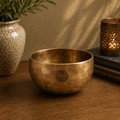 Small Nepalese Moon Bowl - (approx 550g) - 13cm made of brass with a subtle patina, featuring a carved symbol, displayed on a wooden surface with warm ambient lighting.