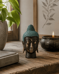 Small Antique Brass Buddha Head with detailed textured hair and serene facial expression, displayed on a wooden surface alongside a lit candle and greenery, creating a peaceful decor.