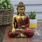 Hand-carved Red & Gold Buddha - Large statue seated in meditation pose, featuring detailed gold and red resin finish, displayed on rustic wooden surface with plants in background.