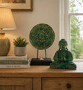 Buddha Feng Shui Set - Buddha Knot - Green displayed on a wooden surface with a decorative lamp, green plant in a gray pot, and stack of books in a cozy, well-lit room.