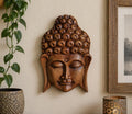 Bali Magic Box - Buddha Head hand carved wooden Buddha wall hanging with serene expression, displayed on a neutral wall near indoor plants and decorative accents.