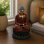 Antique Buddha - Classic Statue in deep red and gold finish seated on a lotus base, displayed on a wooden surface near a window with plants and lit decorative candle nearby.
