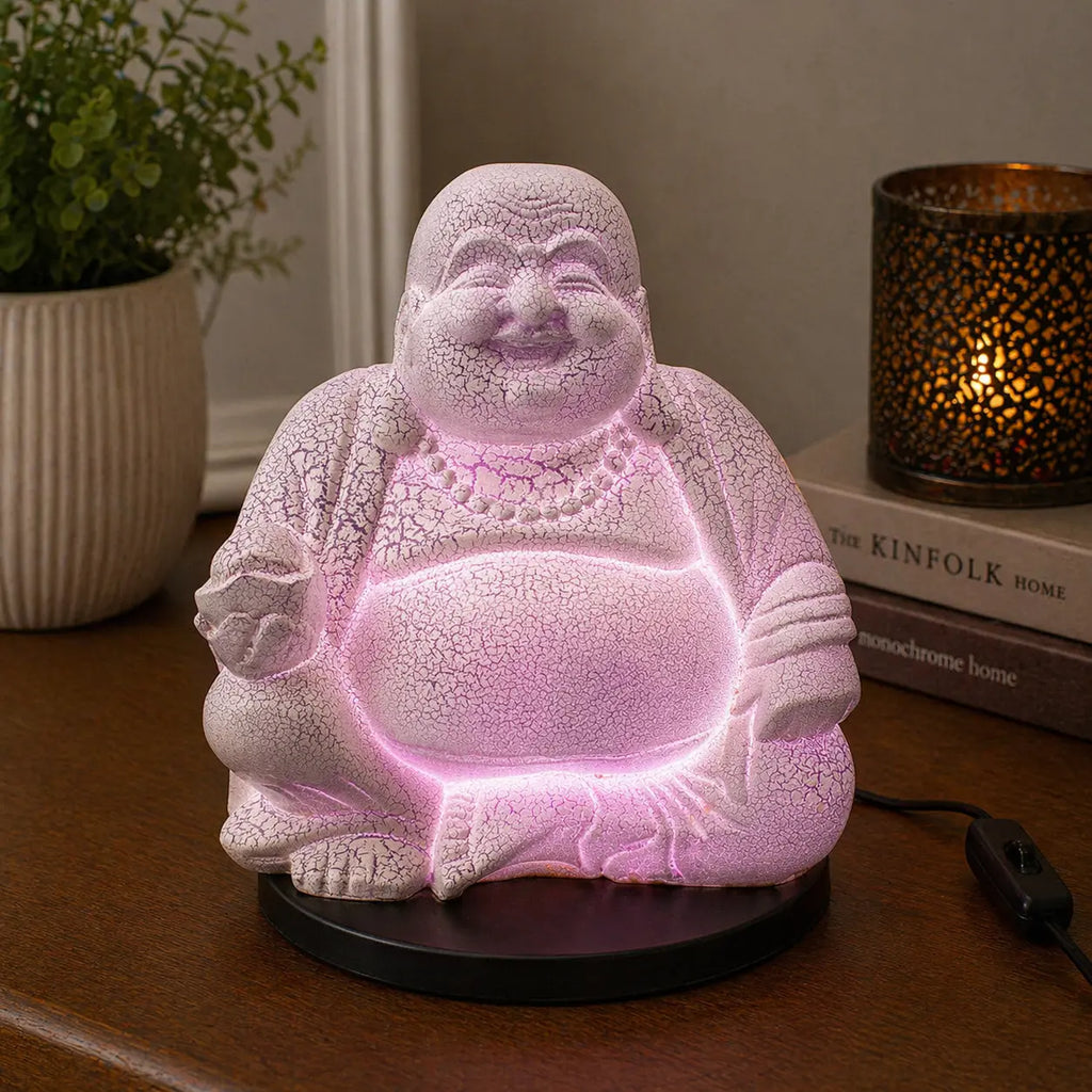 Laughing Buddha Lamp Lavender Crackle - Round Stand glowing softly in lavender light on a wooden surface, featuring a crackled texture and placed next to books and ambient decor.