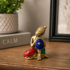 Brass Buddha Figure - Thinking - 6.5 cm sitting on a wooden surface with colorful mosaic inlays in red, blue, and green, surrounded by calm home decor elements.