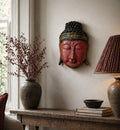 Home Decoration Buddha Head - 25cm - Red Shine Finish mounted on a neutral wall above a rustic wooden table with decorative vase, books, bowl, and lamp creating a serene living space.