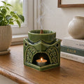 Square Buddha Burner - Dark Jade ceramic oil burner with intricate carved details, lit tealight candle underneath, and incense cone releasing smoke in a cozy indoor setting.