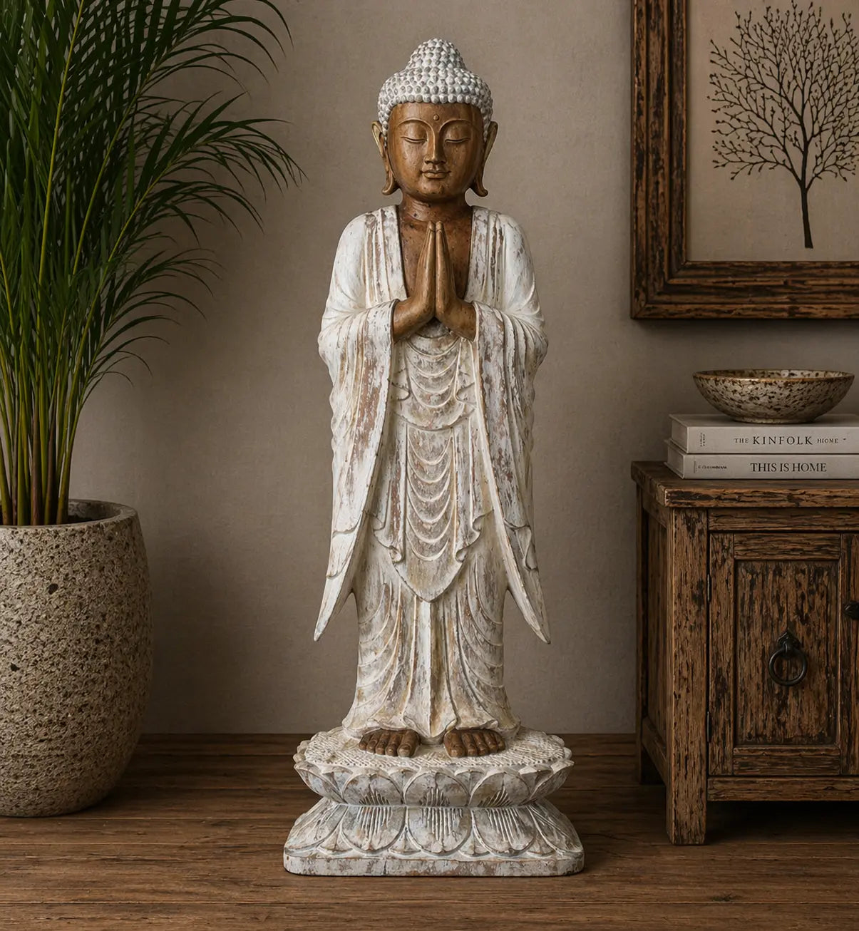Buddha Statue Standing - Whitewash - 1m Welcome displayed indoors on a wooden surface with a serene expression, hands in prayer, standing on a lotus base in rustic decor setting.