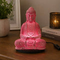 Meditation Buddha Lamp Cherry Crackle - Oval Stand glowing with soft pink light, featuring a crackled finish Buddha statue on a black oval base, placed on a wooden surface with cozy home decor.