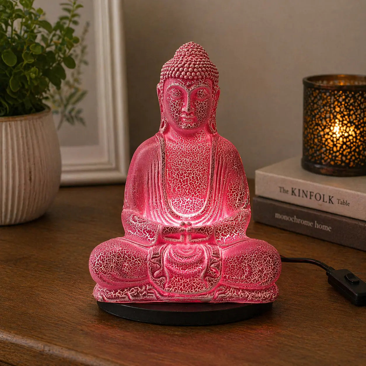 Meditation Buddha Lamp Cherry Crackle - Oval Stand glowing with soft pink light, featuring a crackled finish Buddha statue on a black oval base, placed on a wooden surface with cozy home decor.