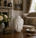 Buddah Head Oil Burner - White made of smooth ceramic with a serene expression, releasing gentle smoke, placed on a wooden table in a cozy, elegantly decorated living room.
