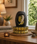 Tabletop Water Feature - 30cm - Golden Buddha & Vitarka Mudra displayed on a wooden surface with a peaceful home decor setting, including a lit candle and green plants.