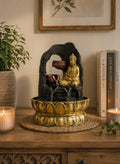 Tabletop Water Feature - 30cm - Golden Meditating Buddha with flowing water in a decorative lotus-shaped base, placed on a wooden surface beside candles and books.