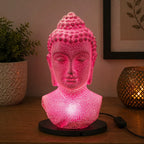 Buddha Bust Lamp Cherry Crackle - Oval stand glowing with soft pink light, featuring a textured crackle finish on a serene Buddha head sculpture on an oval black base.