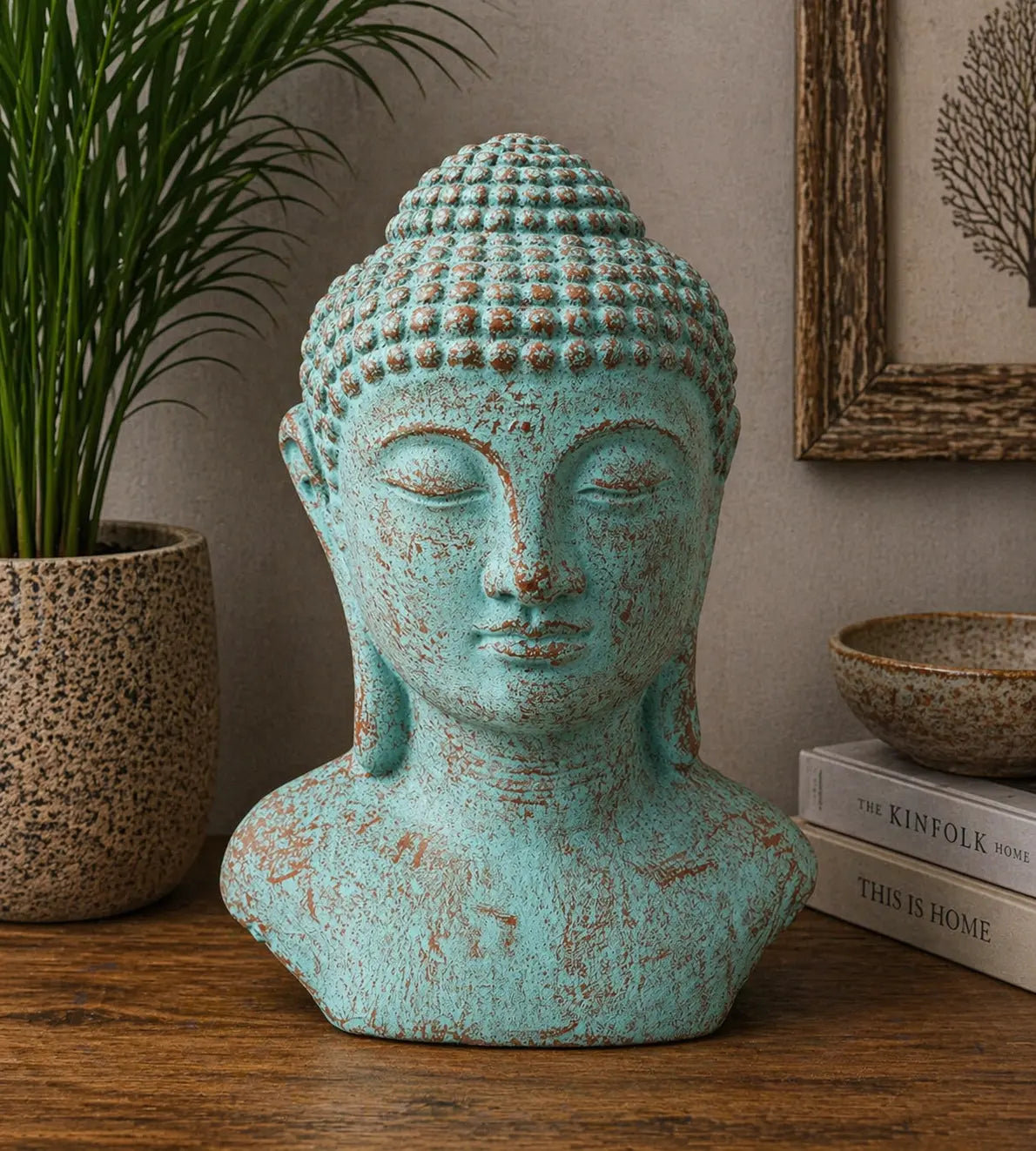 Tranquility Buddha Head - Green Copper statue with a serene expression, featuring a rustic green copper finish, displayed on a wooden surface with modern decor elements.