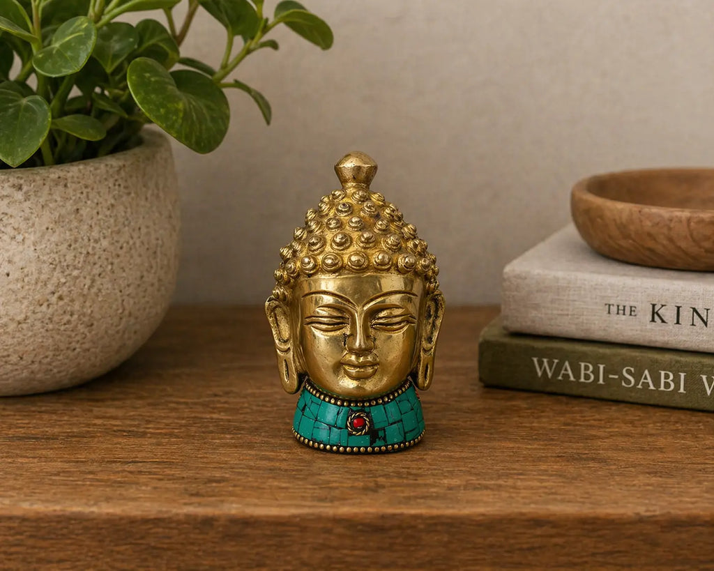 Brass Buddha Figure - Med Head - 8 cm with intricate curls and closed eyes, featuring turquoise and red stone accents, displayed on a wooden surface with books and a plant nearby.