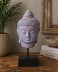 Stillness Buddha Head on Stand - Blue Copper displayed on a black base, featuring a textured blue copper finish with serene facial details, surrounded by rustic home decor.