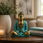 Teal & Gold Buddha - Medium seated hand carved Buddha statue in serene meditation pose with teal robe and gold accents, displayed on wooden table beside books and candle.