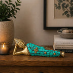 Brass Buddha Figure - Lying Down - 10cm with turquoise mosaic inlay, displayed on a wooden surface beside a candle and potted plant, creating a peaceful and decorative ambiance.