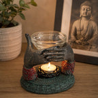Antique Buddha - Offering Hands Oil Burner with detailed hand sculpture holding a glass bowl above a lit tealight candle, styled in a serene decorative setting.
