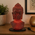 Buddha Bust Lamp Molton Lava - Oval stand casting a warm red glow, featuring a textured lava finish on a black oval base, positioned on a wooden surface near decorative items.