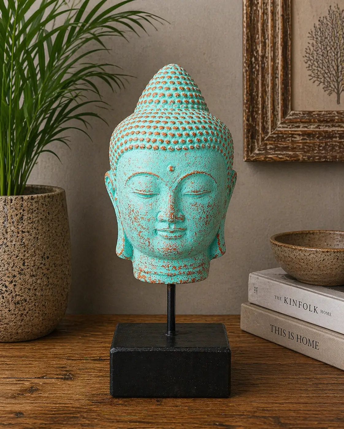 Stillness Buddha Head on Stand - Green Copper displayed on a black stand, featuring a serene Buddha face with aged green copper patina, styled in a calming home decor setting.