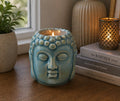 Buddha Oil Burner - Blue ceramic oil burner shaped like a serene Buddha head, placed on a wooden surface near books and decorative candles for calming home decor.