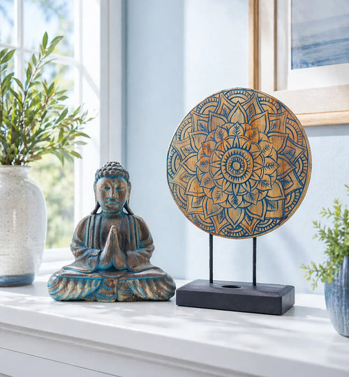 Buddha Feng Shui Set - Flower Mandala - Blue featuring a seated Buddha statue with hands in prayer and a decorative flower mandala on a stand, displayed on a white surface with plants and artwork in the background.