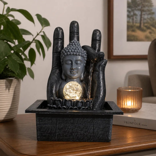 Buddha Hand & Head Tabletop Water Feature (20x25x35cm) with a serene Buddha head resting against a large hand, featuring a glowing orb and flowing water on a wooden table.