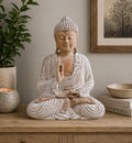 Buddha Statue Whitewash - 40cm Teaching Transmission seated on a wooden surface with rustic whitewashed finish, surrounded by minimalist home decor including a plant, candle, books, and a framed tree print.