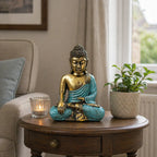 Teal & Gold Buddha - Large seated on a wooden table next to a lit candle and a potted plant, featuring detailed hand-painted resin Buddha statue perfect for peaceful Buddha decor.