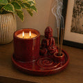 Multi Purpose Buddha Incense Plate - Ceramic Soft Red featuring a soft red ceramic Buddha statue, incense holder with burning incense sticks, and a two-wick candle on a round plate.