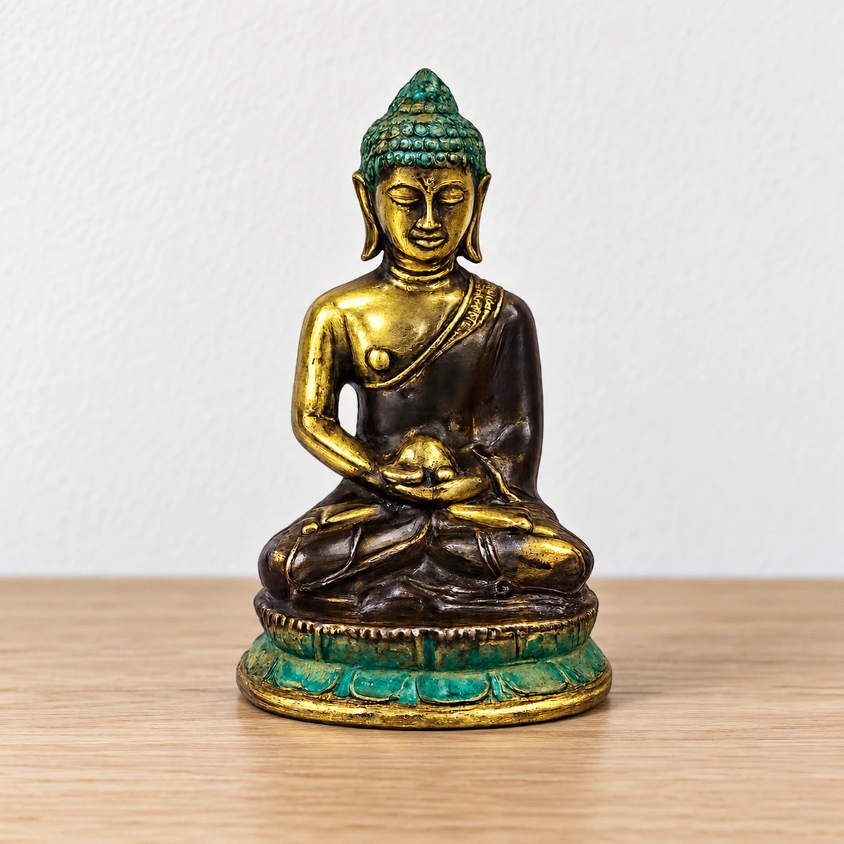 Med Meditation Sitting Brass Buddha Figure, centred on a bare oak surface against a white wall.